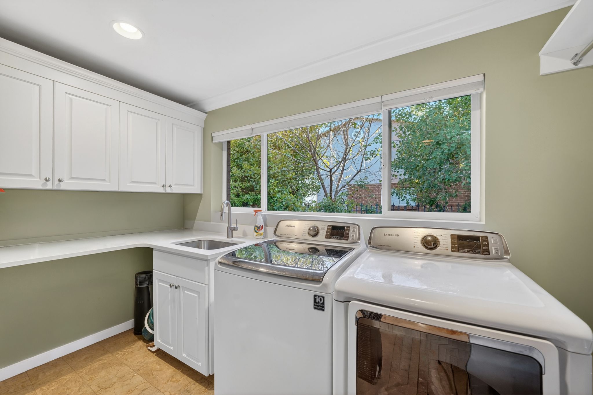 Laundry room featuring white shaker cabinetry, an integrated sink with a stainless steel faucet, ample counter space, and a large window
