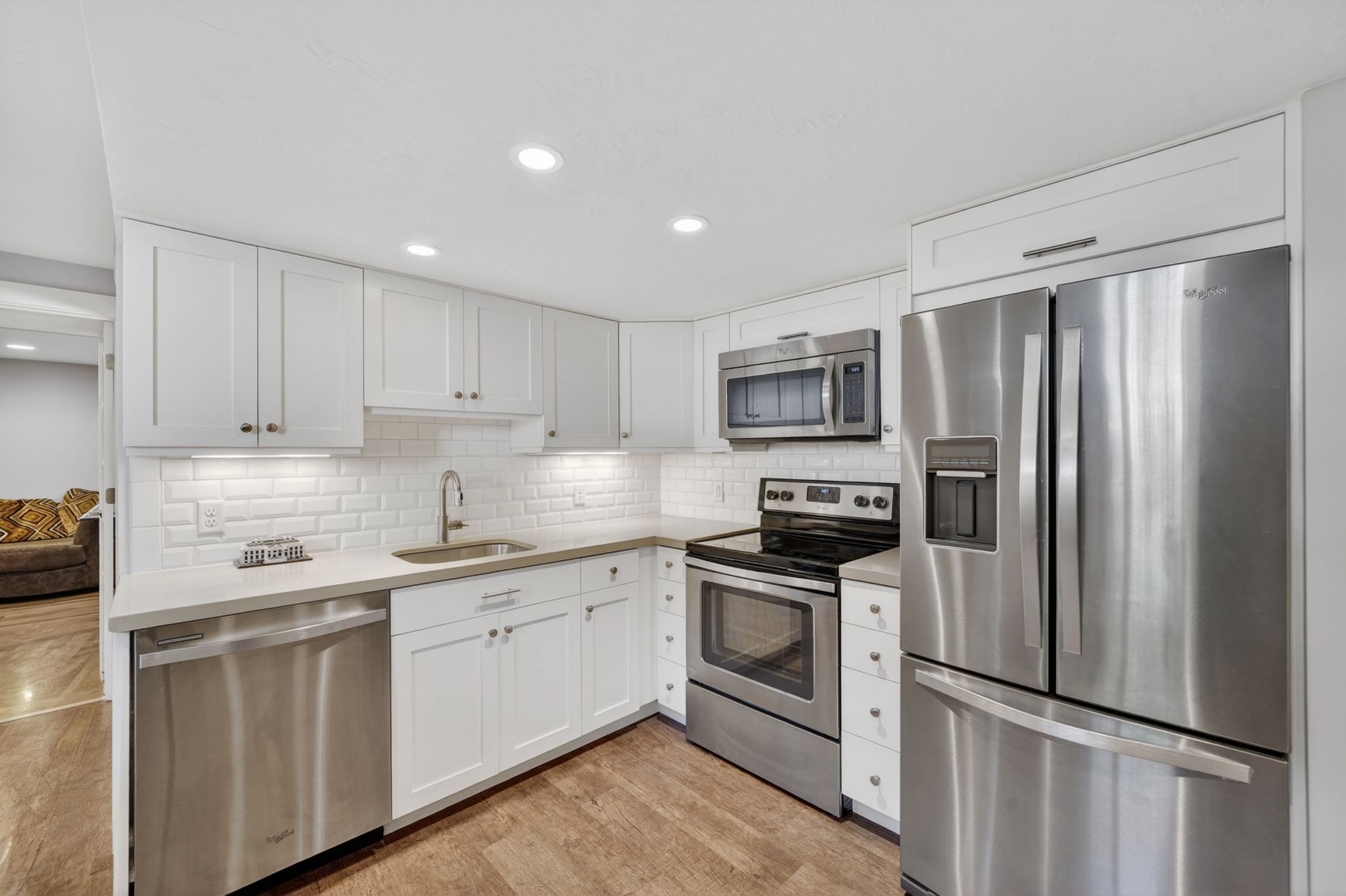 Modern kitchen featuring white shaker cabinetry, stainless steel appliances, light countertops, subway tile backsplash, and wood-finish flooring