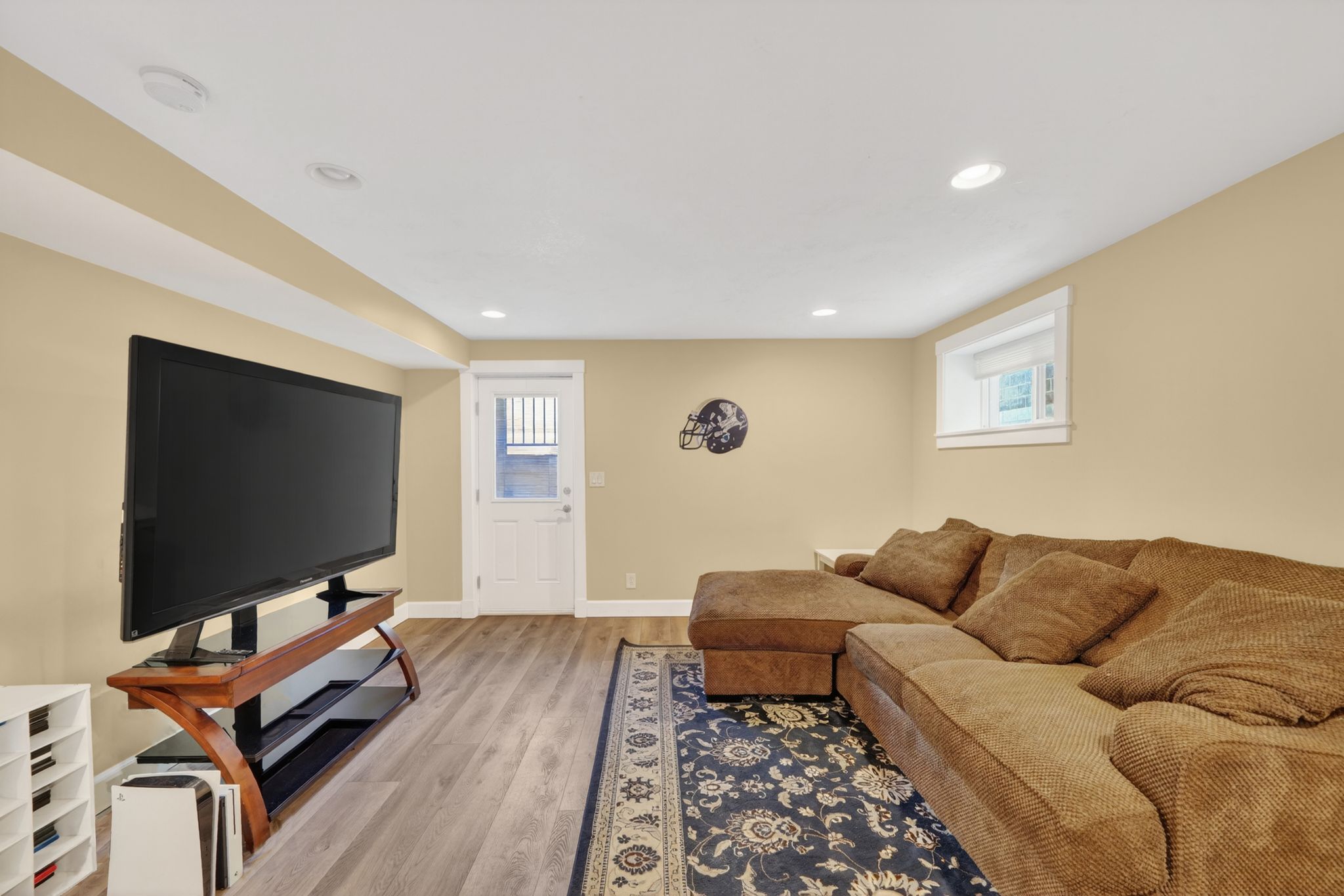 Finished lower level featuring wood-finish flooring, recessed lighting, a white painted trim package, an egress window, and a white paneled door
