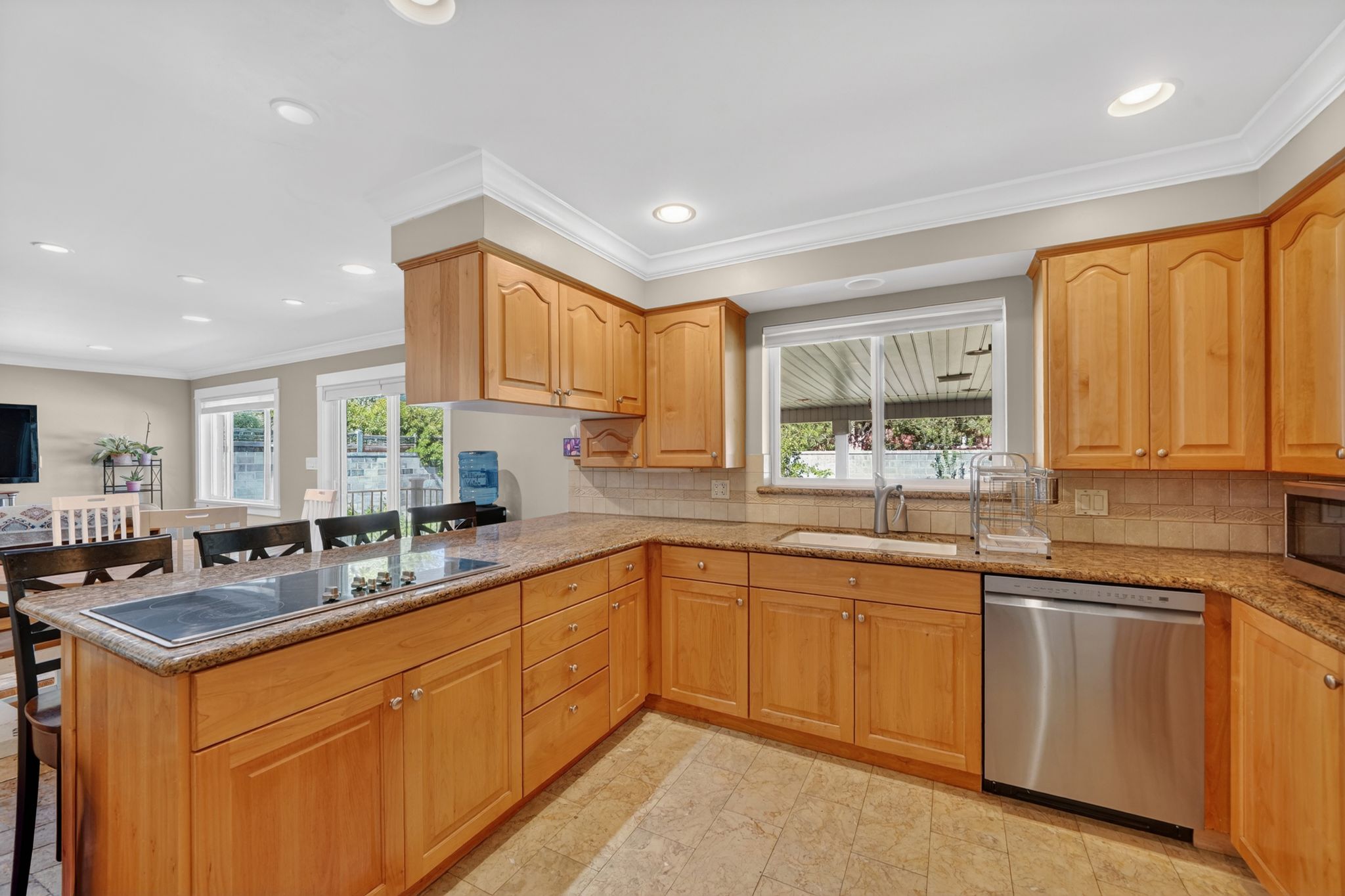 Kitchen featuring light wood cabinetry, granite-style countertops, stainless steel dishwasher, and an integrated cooktop on the island