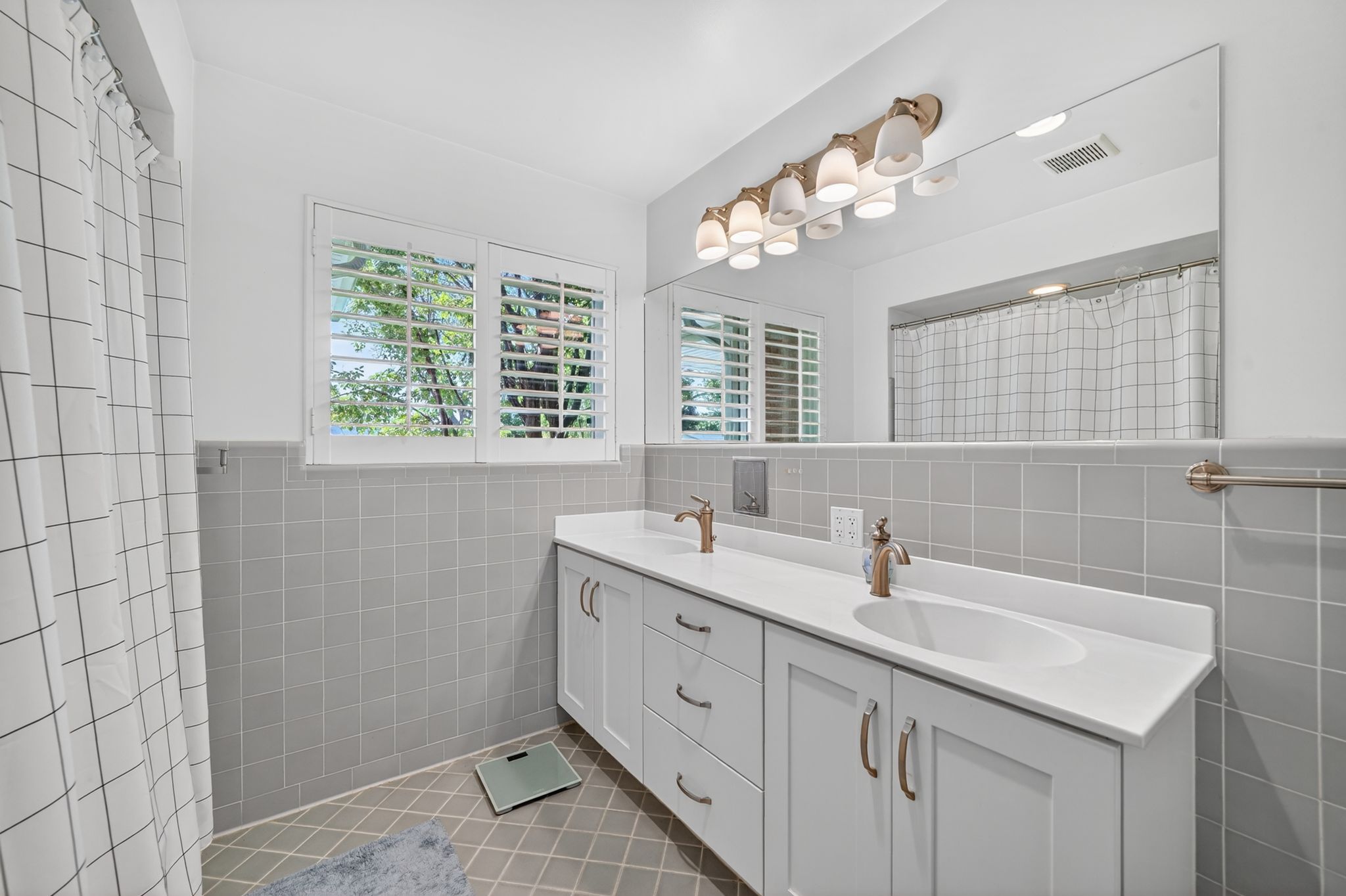 Bathroom featuring a double vanity with white cabinetry and integrated sinks, brushed bronze hardware, and a large wall-mounted mirror