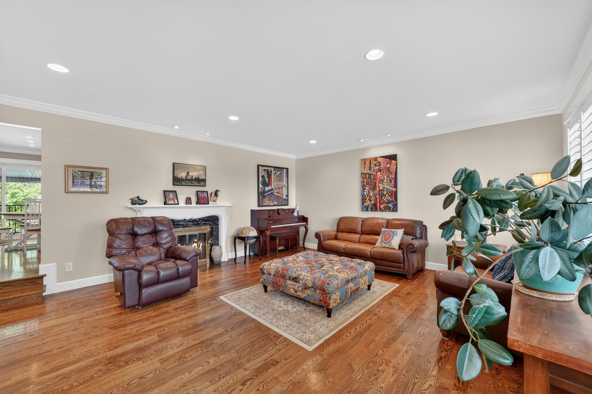 Spacious living area featuring polished wood-finish flooring, a white mantel fireplace, recessed lighting, and crown molding