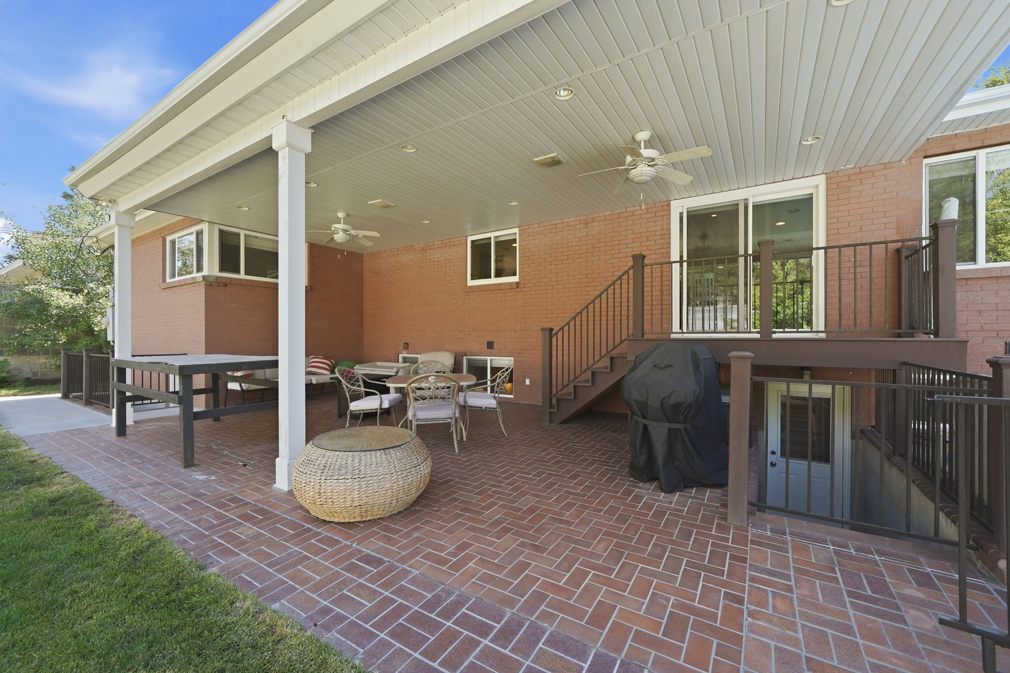 Expansive covered patio featuring brick pavers, white columns, and a beadboard ceiling with recessed lighting and ceiling fans