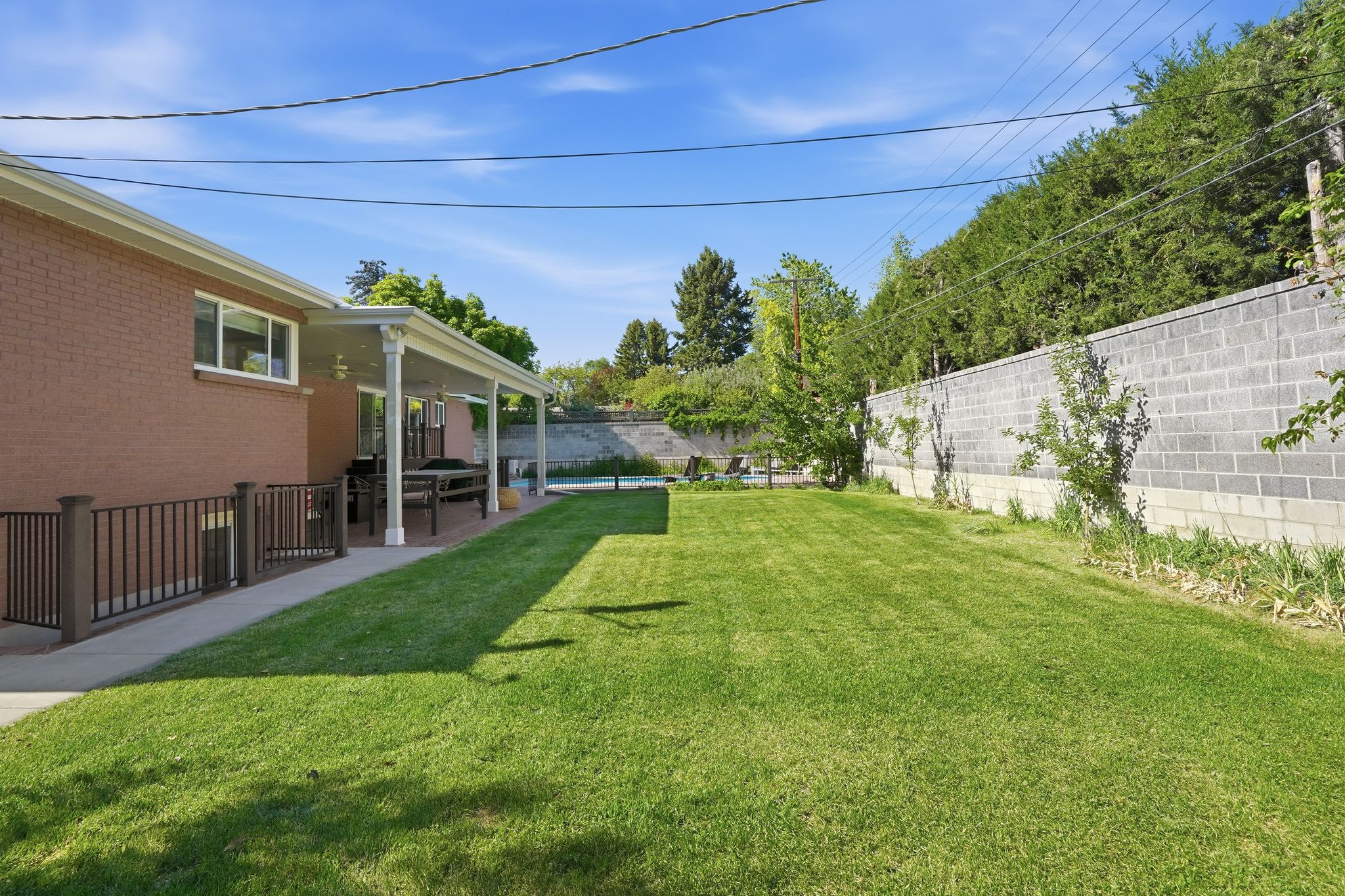 Expansive green lawn with a covered patio, brick exterior, and privacy wall