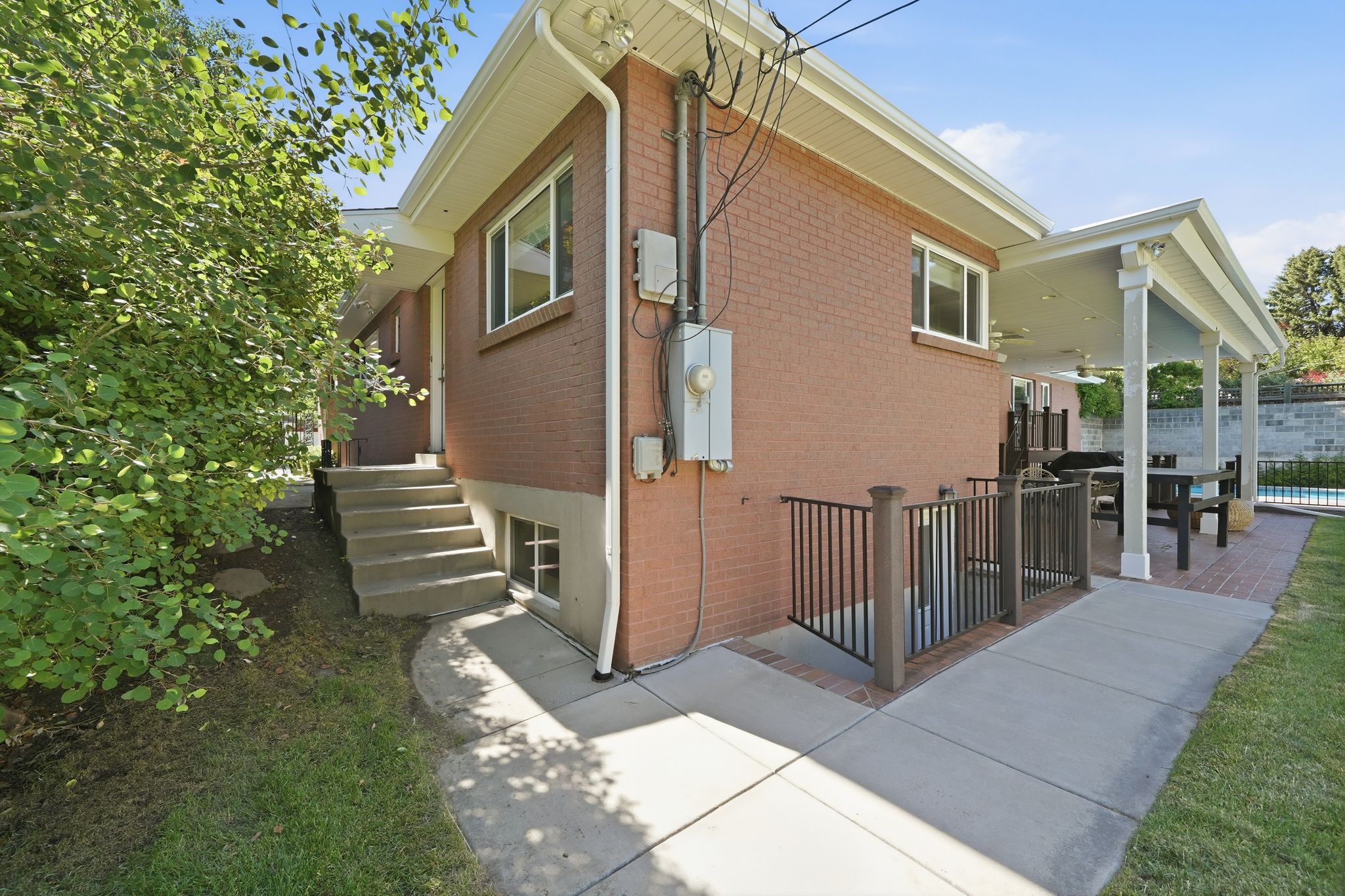 Brick exterior with a covered patio, featuring a built-in outdoor kitchen area, a concrete pathway, a fenced lower-level entry, and a manicured lawn
