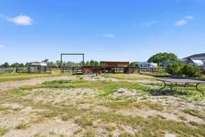 Expansive open space featuring a metal gate, multiple wooden structures, and a detached shed
