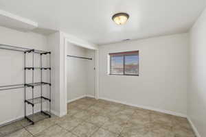 Room featuring neutral wall tones, square tile flooring, a window with horizontal blinds, and a flush-mount ceiling light