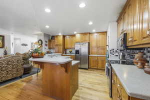 Kitchen featuring wood cabinetry, stainless steel appliances, a black and white tiled backsplash, light-toned countertops, and wood-finish flooring
