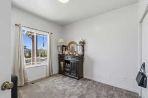 Well-lit room featuring a large window with white trim, neutral wall paint, and textured carpet flooring