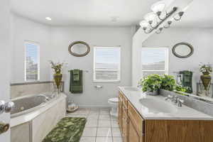 Bathroom featuring a built-in jetted tub with a marble surround, dual vanity with wood-finish cabinetry and integrated sinks, a wide mirror, and tiled flooring