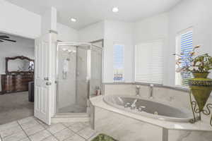 Spacious bathroom featuring a corner soaking tub, separate glass-enclosed shower, white tile flooring, and multiple windows with blinds