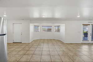 Open living area featuring neutral tile flooring, a bay window with blinds, and white painted walls
