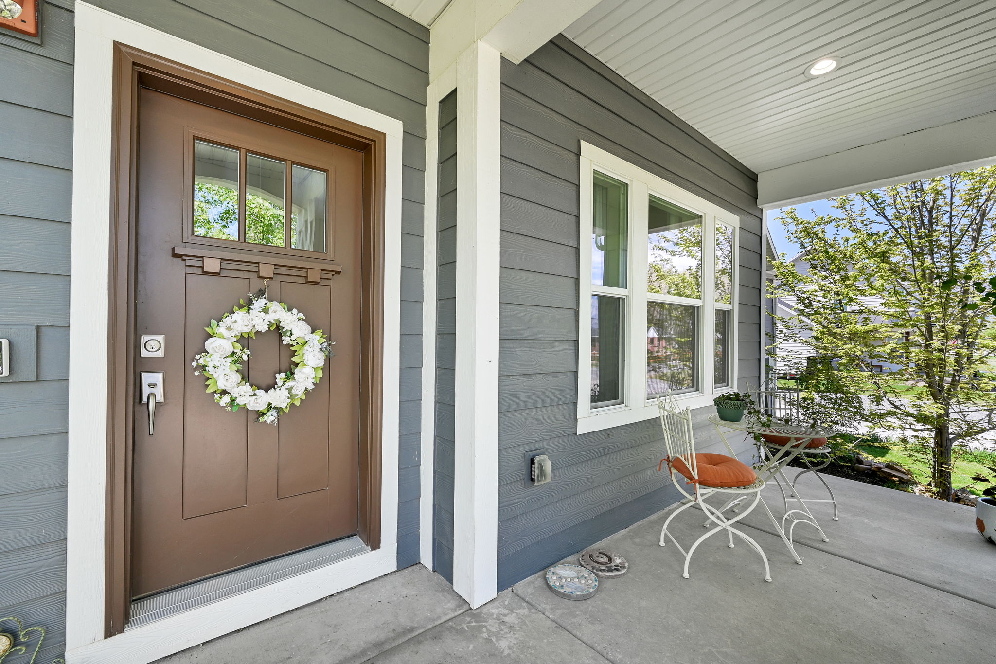 Inviting front porch featuring a brown entry door with transom window, gray horizontal siding, and white trim accents