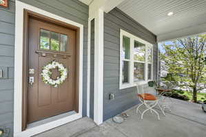 Inviting front porch featuring a brown entry door with transom window, gray horizontal siding, and white trim accents