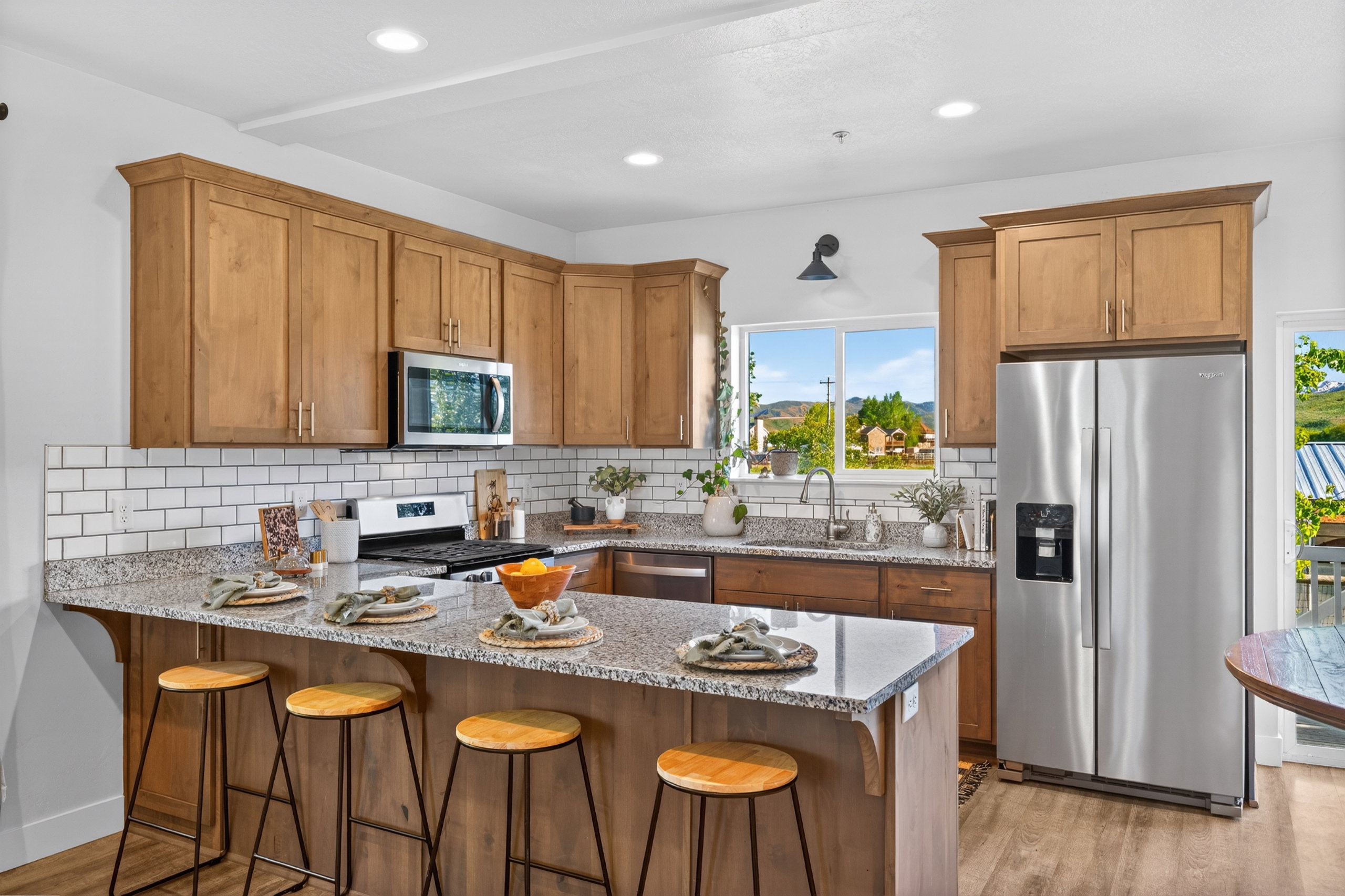 Kitchen featuring wood-finish cabinetry, stainless steel appliances, speckled stone countertops, a subway tile backsplash, and an island with bar seating
