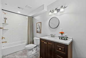 Bathroom featuring a white subway tile shower surround with gold-finish fixtures, a dark wood-finish vanity with a light-colored countertop, and a round wall mirror