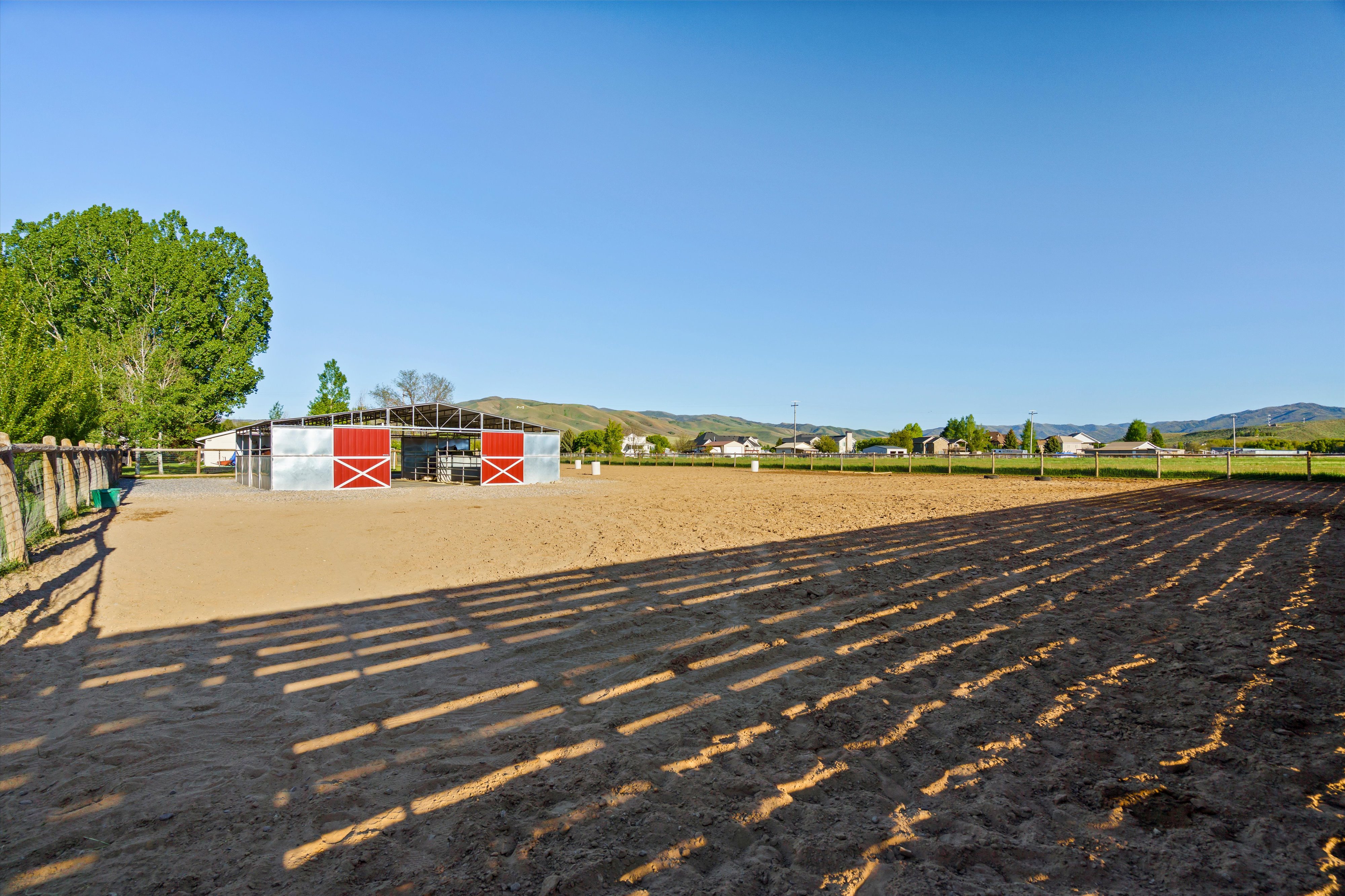 Expansive outdoor riding arena featuring a perimeter fence and a metal-clad barn with red sliding doors