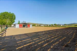 Expansive outdoor riding arena featuring a perimeter fence and a metal-clad barn with red sliding doors