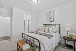 Spacious room featuring light wood-finish flooring, crisp white walls, a doorway to an additional space, and a ceiling-mounted light fixture