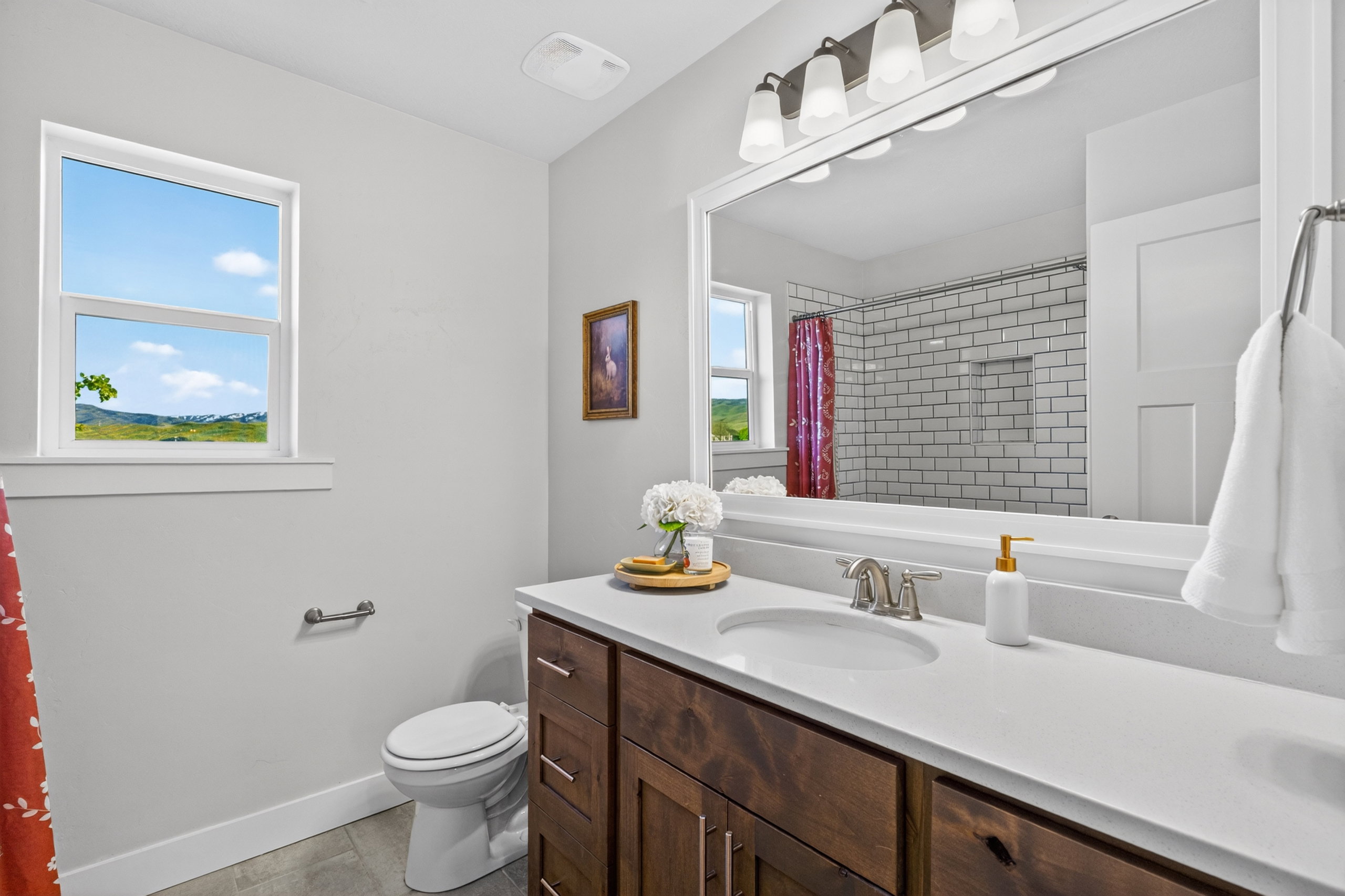 Bathroom featuring a single window, a dark wood-finish vanity with a light countertop, a built-in sink, and a large mirror with overhead lighting