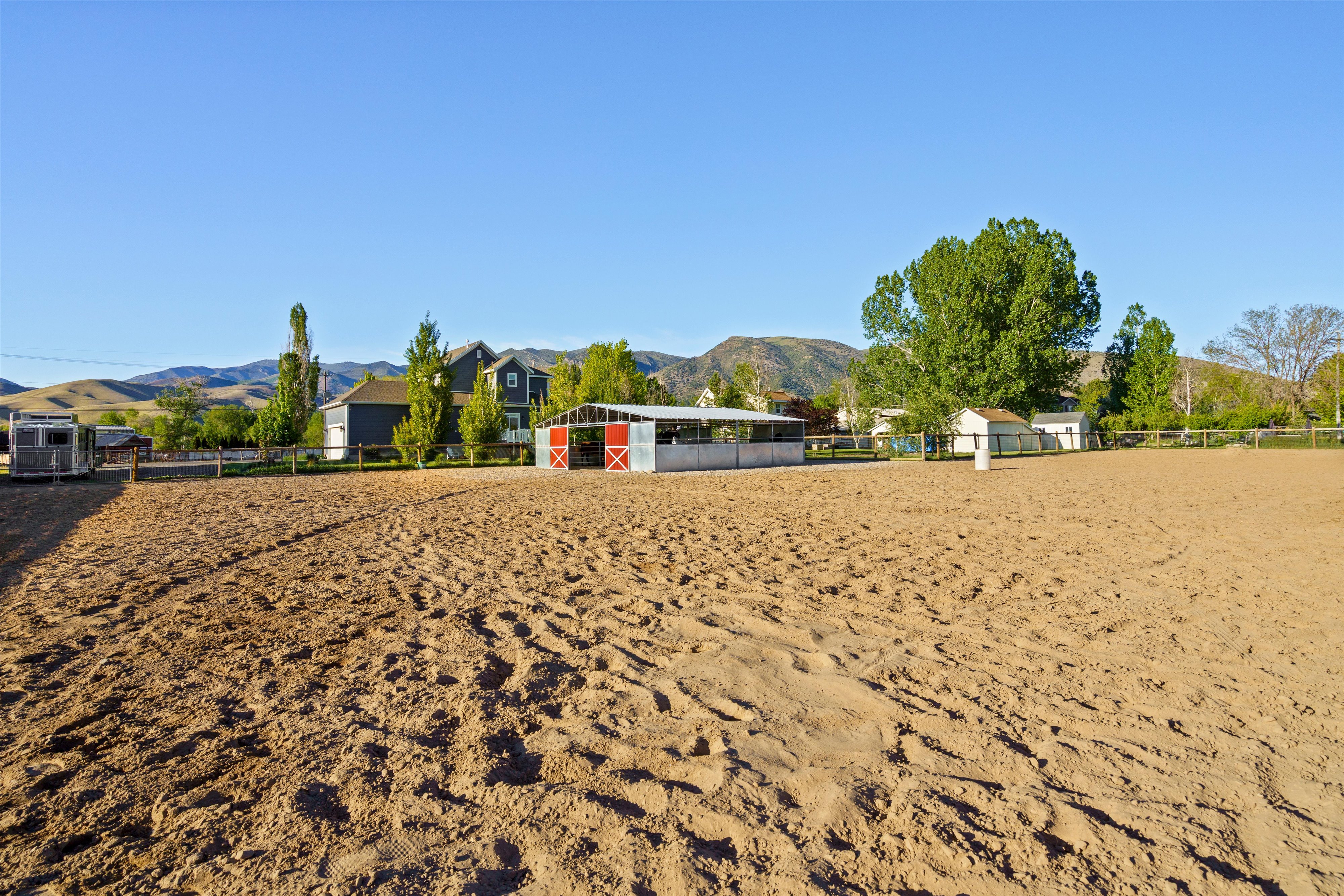 Expansive equestrian arena featuring a sand surface, a white-fenced perimeter, and a detached barn structure with red-painted doors