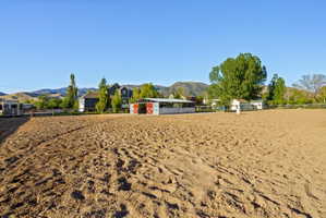 Expansive equestrian arena featuring a sand surface, a white-fenced perimeter, and a detached barn structure with red-painted doors
