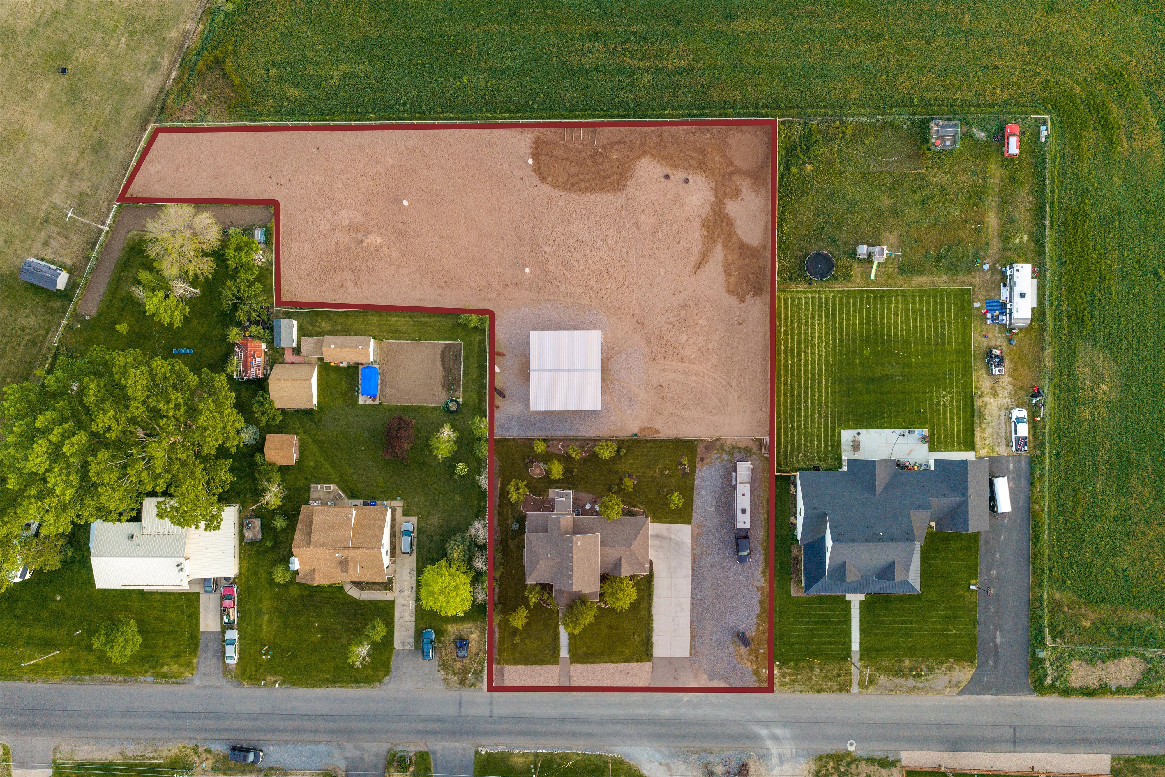 Expansive land parcel featuring a main residence with a dark-pitched roof, a large gravel lot, a substantial open-sided structure, a secondary residence with a light-colored roof, and a well-maintained lawn