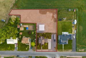 Expansive land parcel featuring a main residence with a dark-pitched roof, a large gravel lot, a substantial open-sided structure, a secondary residence with a light-colored roof, and a well-maintained lawn