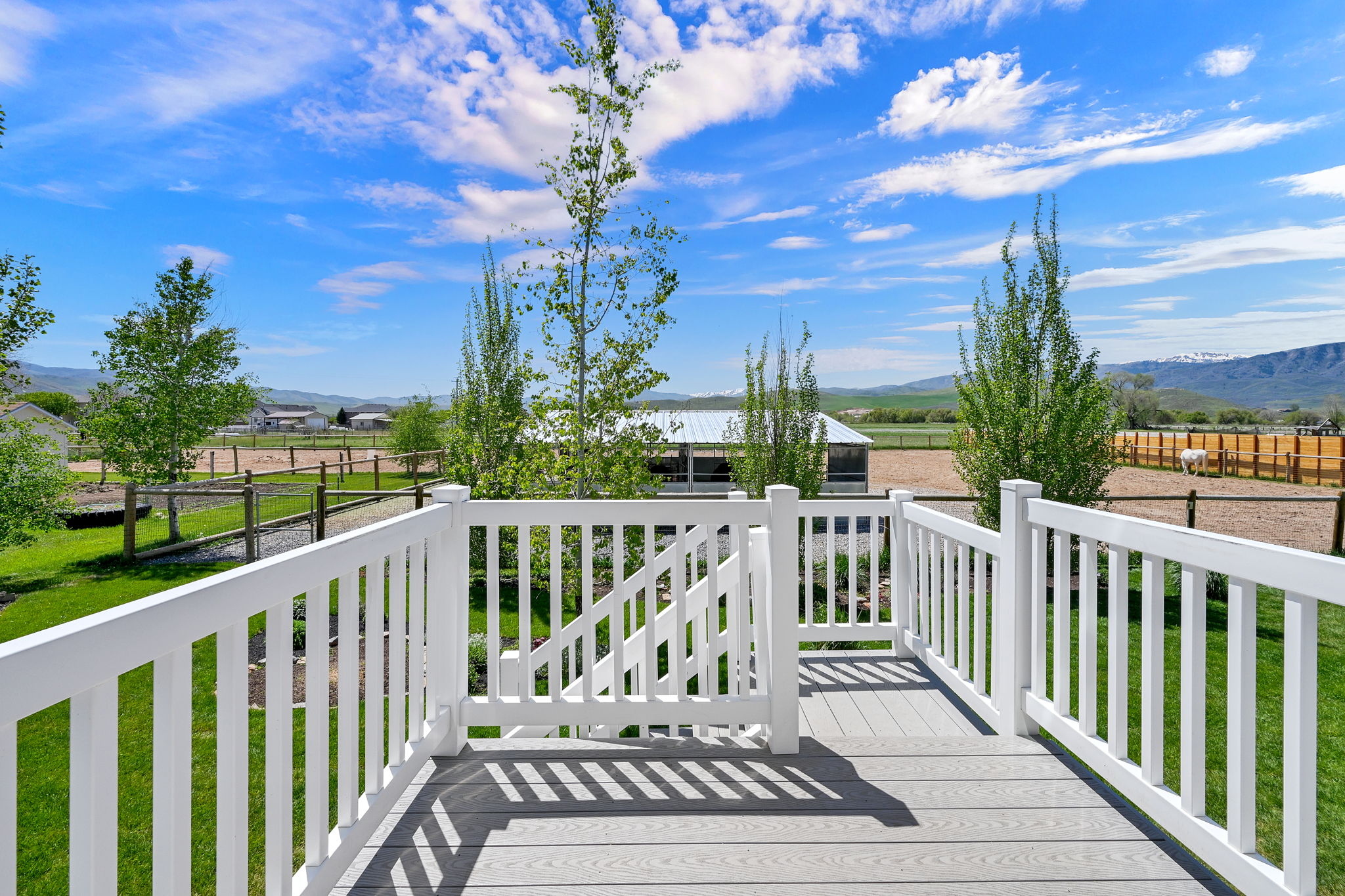 Composite deck with white railings and gate overlooking horse barn and pasture.