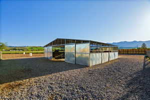 Open-air metal barn structure with multiple stalls, a gravel-surfaced paddock, and an adjacent dirt arena