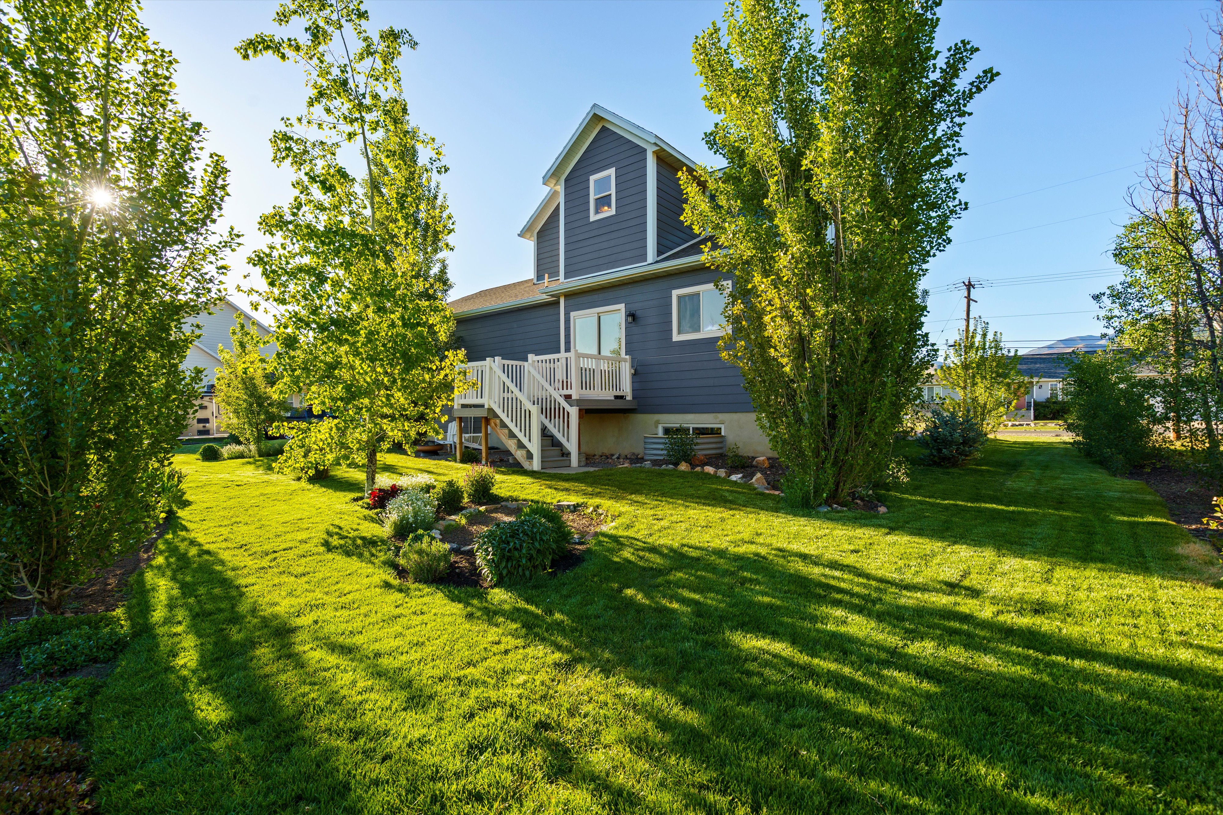 Spacious rear yard featuring a verdant lawn, mature trees, and established garden beds