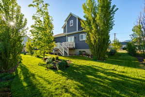 Spacious rear yard featuring a verdant lawn, mature trees, and established garden beds