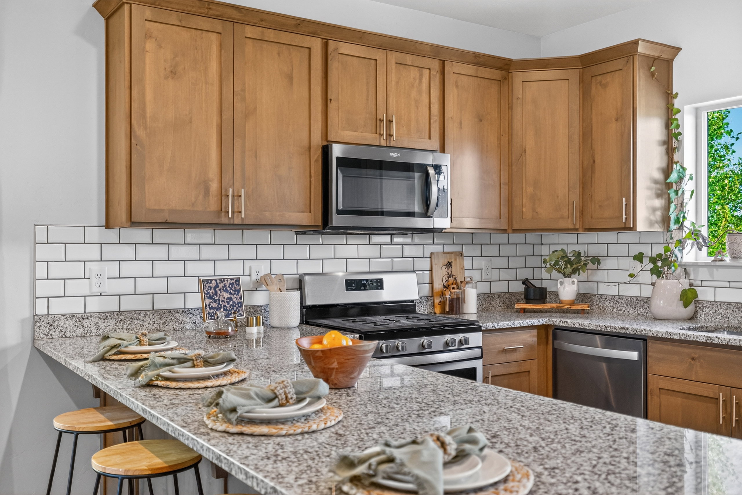 Kitchen featuring wood cabinetry, a white subway tile backsplash, granite countertops, stainless steel appliances, and a breakfast bar