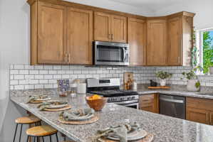 Kitchen featuring wood cabinetry, a white subway tile backsplash, granite countertops, stainless steel appliances, and a breakfast bar
