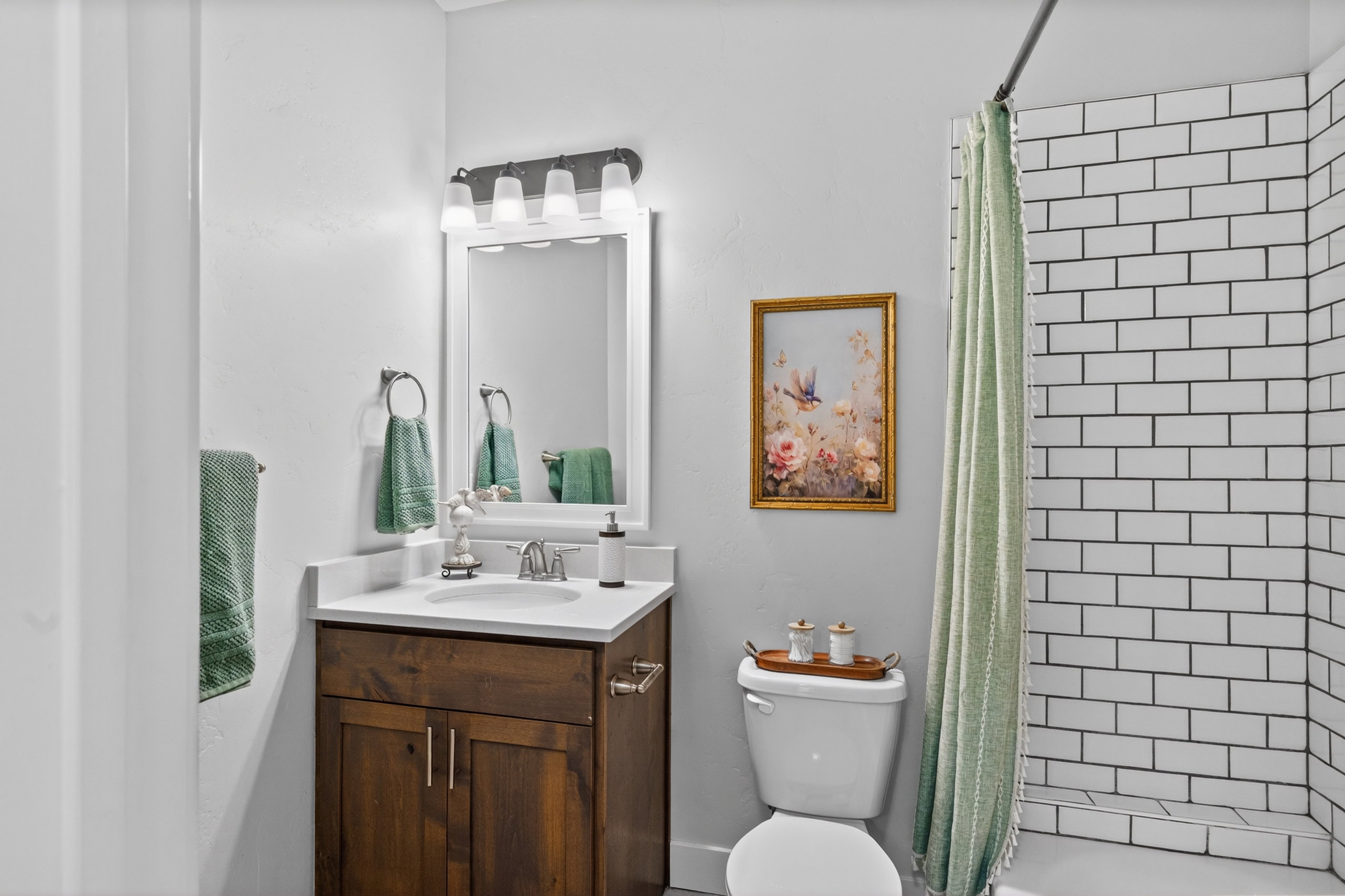 Bathroom featuring a white subway tile shower, wood-finish vanity with countertop, and framed mirror with integrated lighting