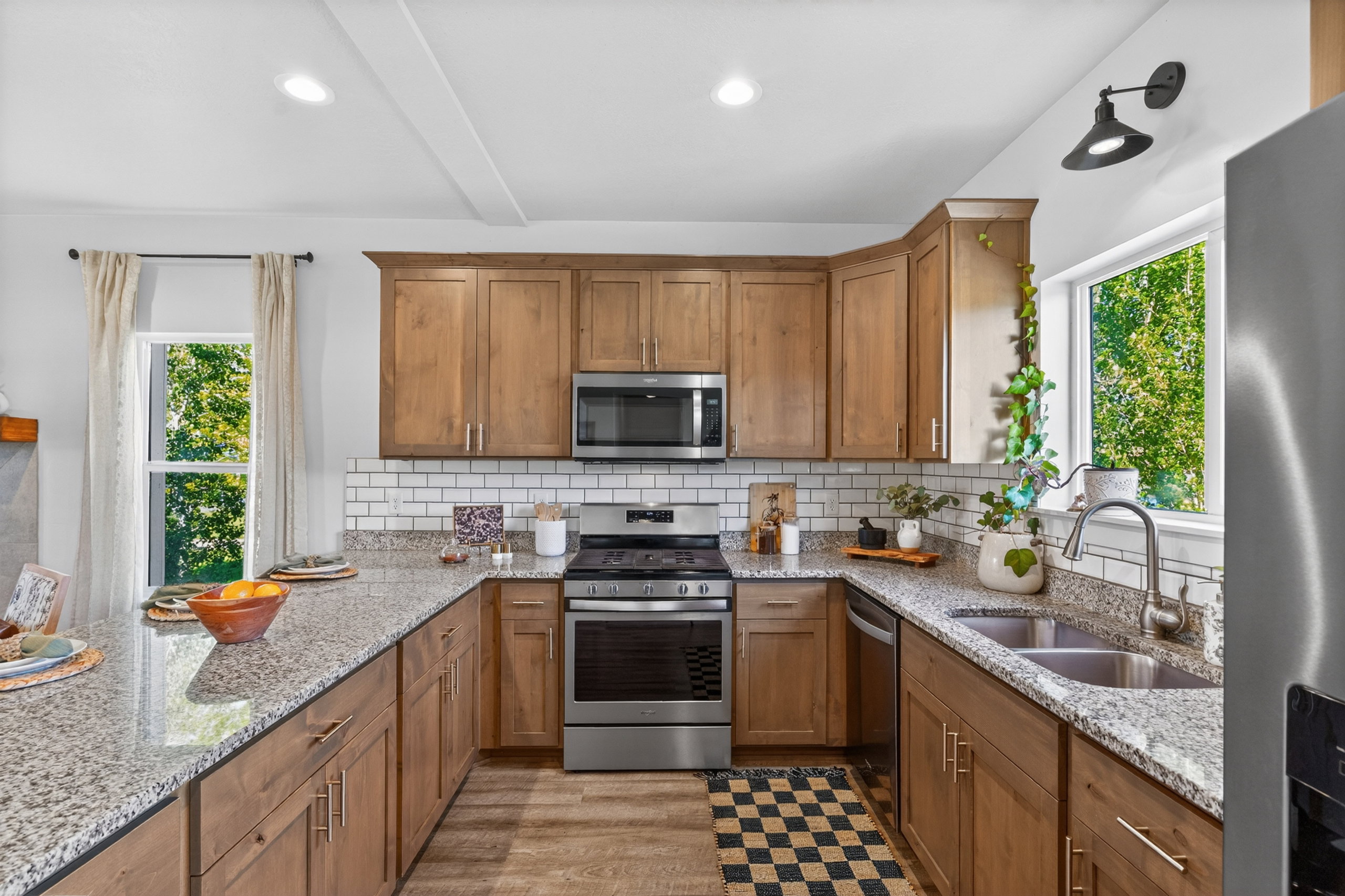 U-shaped kitchen featuring wood cabinetry, stainless steel appliances, granite countertops, and a subway tile backsplash