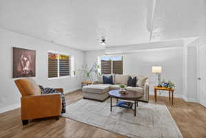 Spacious living area featuring wood-finish flooring, light-toned walls, and recessed windows with horizontal blinds