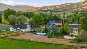 Expansive property featuring a large white residence with a dark roof, a spacious unpaved yard, a wood fence, and a clear span building