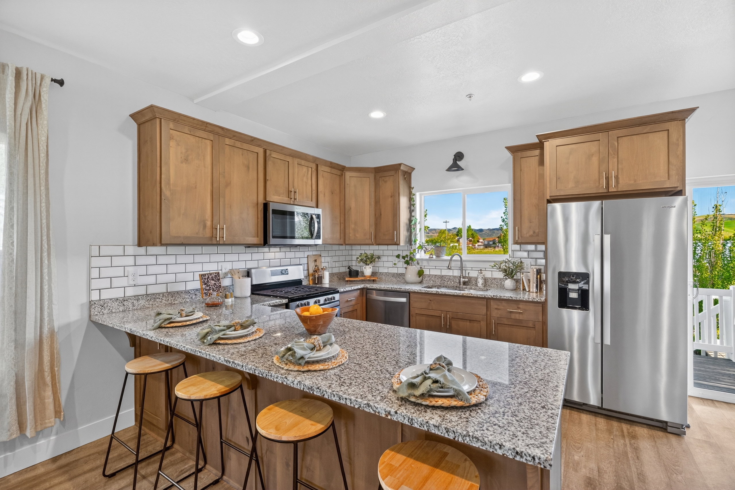 Kitchen featuring a granite-topped island with seating, wood-finish flooring, stainless steel appliances, and subway tile backsplash