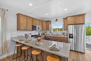 Kitchen featuring a granite-topped island with seating, wood-finish flooring, stainless steel appliances, and subway tile backsplash