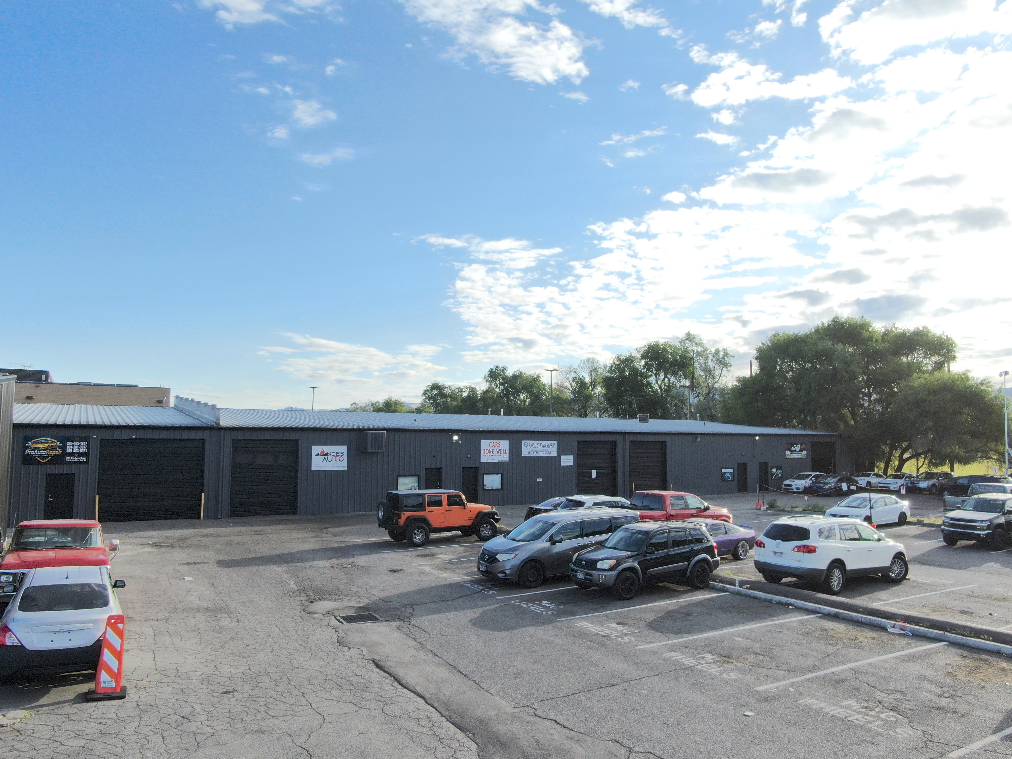 Commercial building featuring multiple large bay doors, a corrugated metal roof, and an expansive paved lot