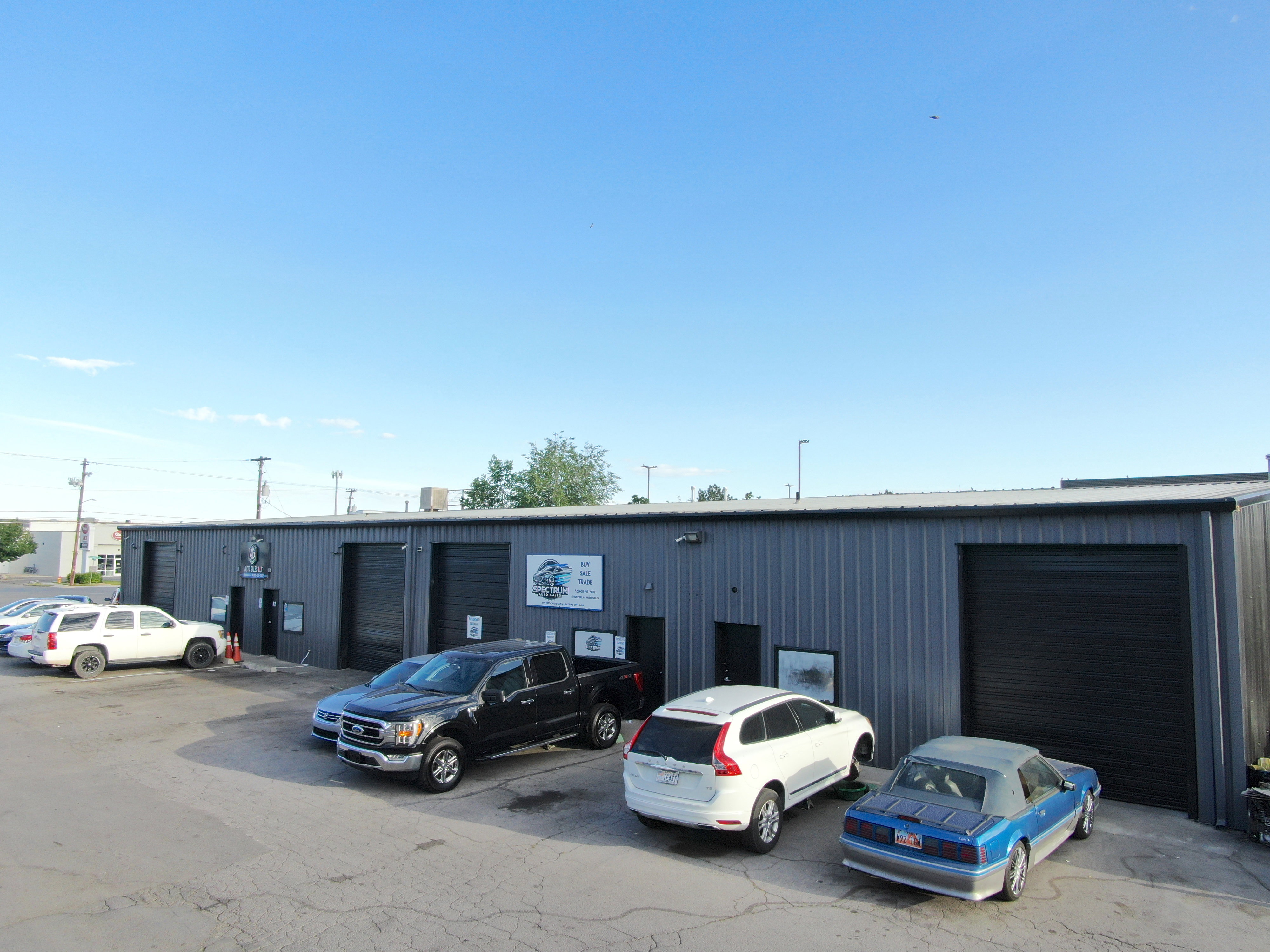 Commercial property featuring a gray corrugated metal exterior, multiple black roll-up garage doors, a flat roofline, and a paved parking area
