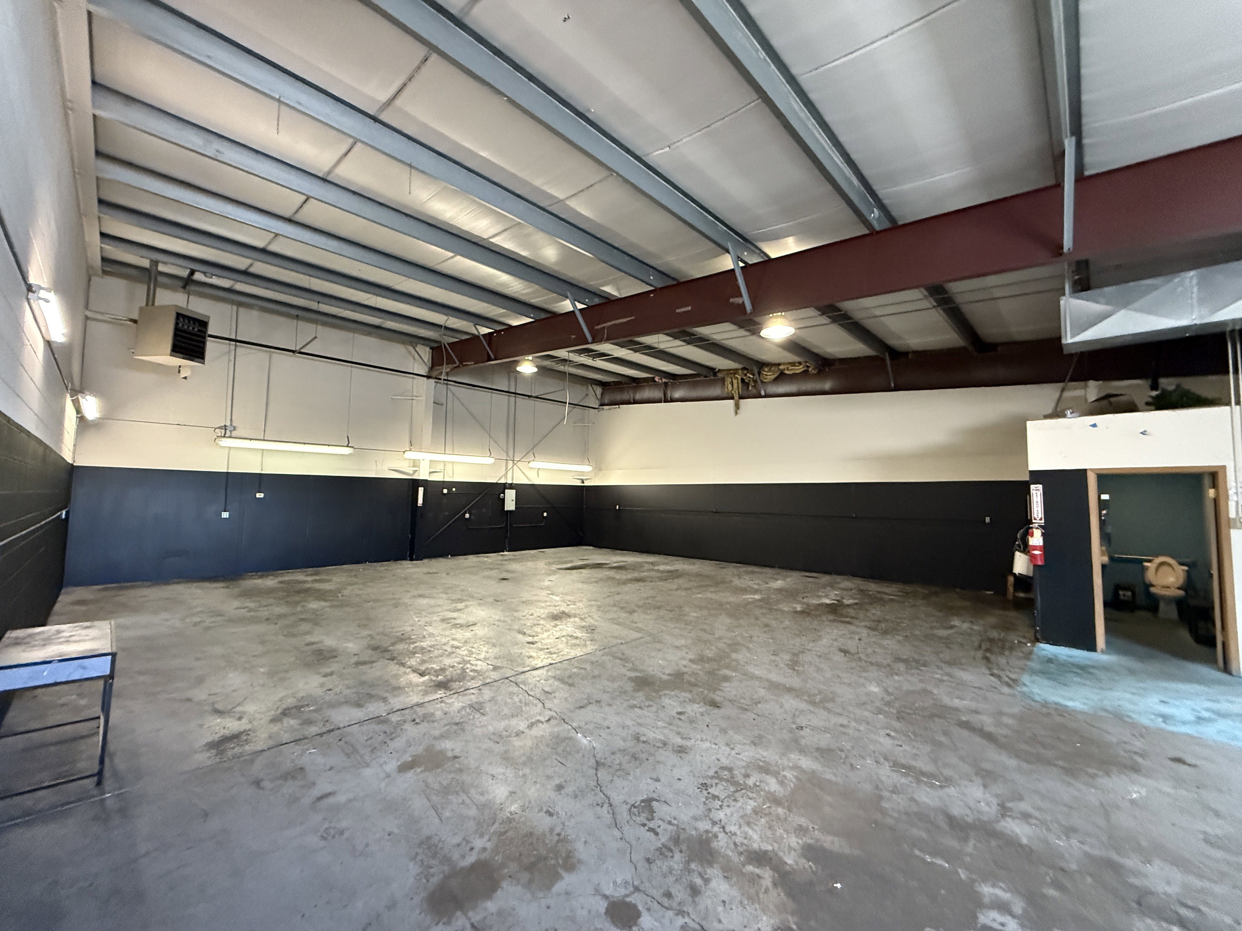 Spacious industrial interior featuring an exposed metal beam ceiling with fluorescent lighting