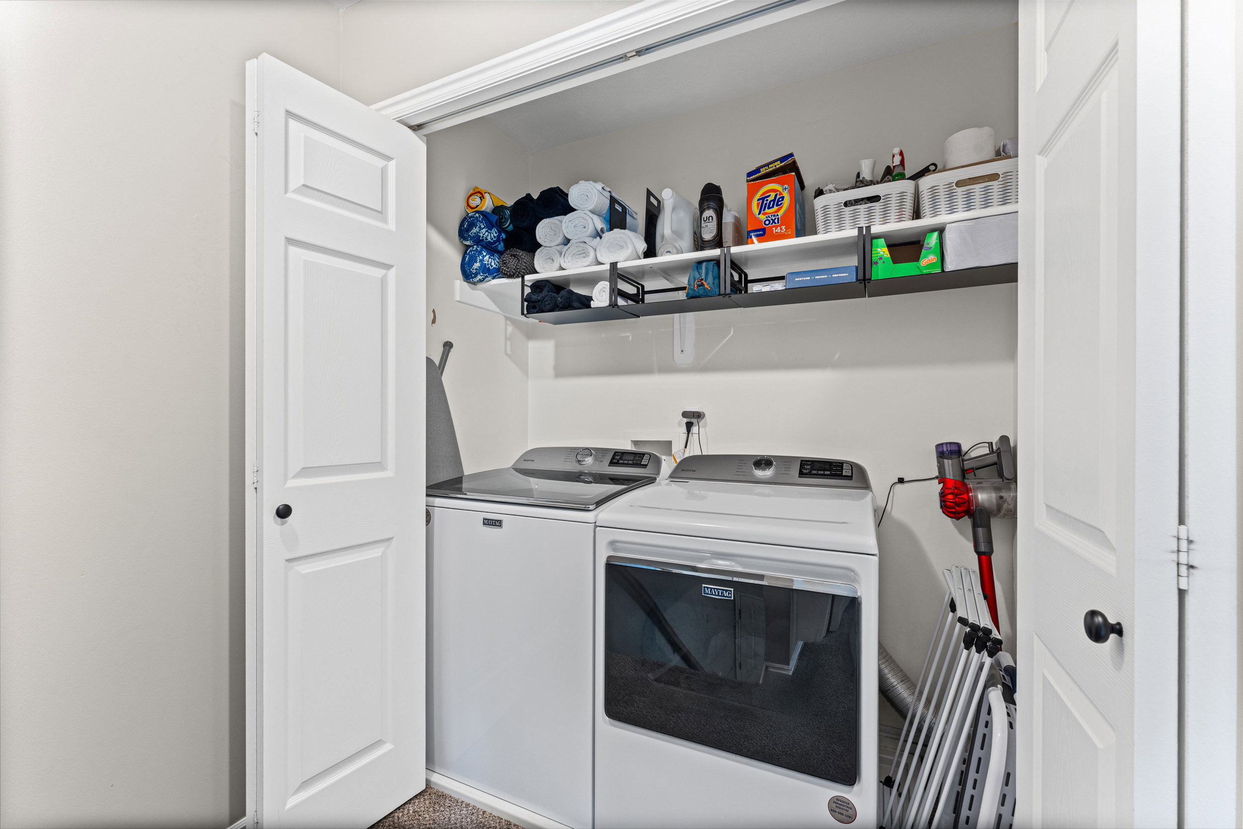 Dedicated laundry closet with white panel doors, overhead shelving, and neutral wall tones