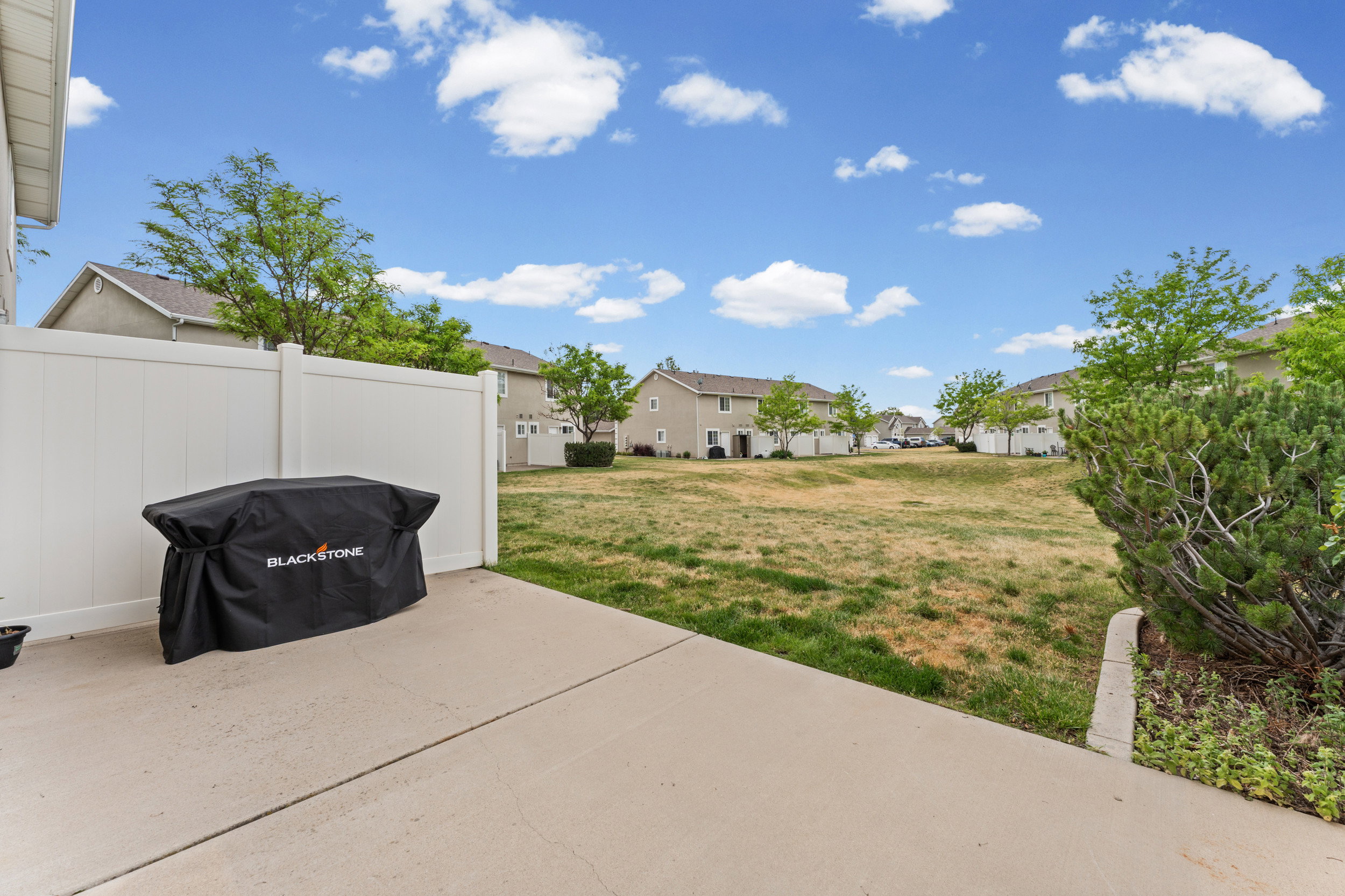 Concrete patio area featuring a white vinyl privacy fence and an open grass field beyond