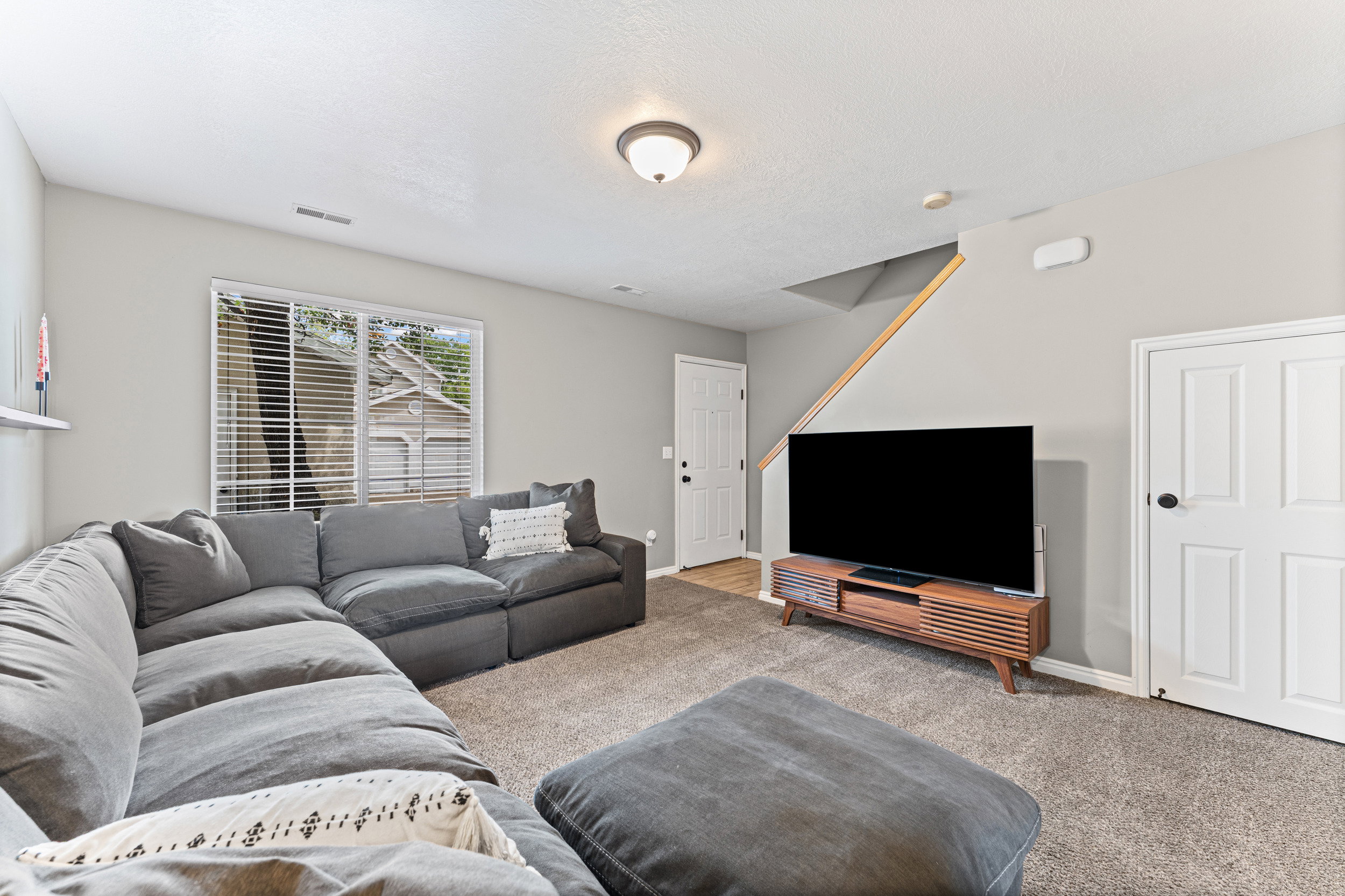 Carpeted living area featuring light gray walls, a window with blinds, and a built-in shelf