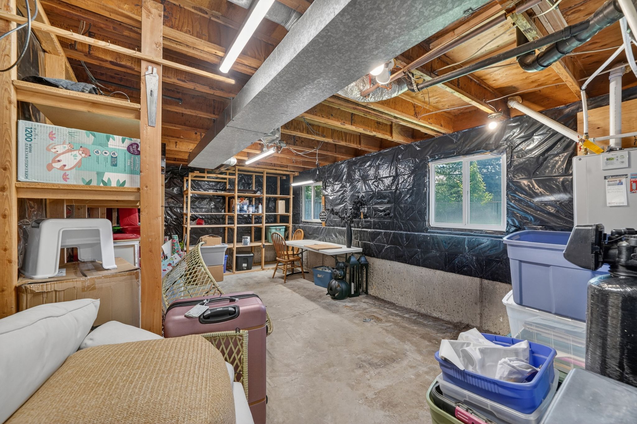 Unfinished basement featuring exposed wood joists, concrete flooring, built-in shelving, two windows, and an exposed HVAC duct