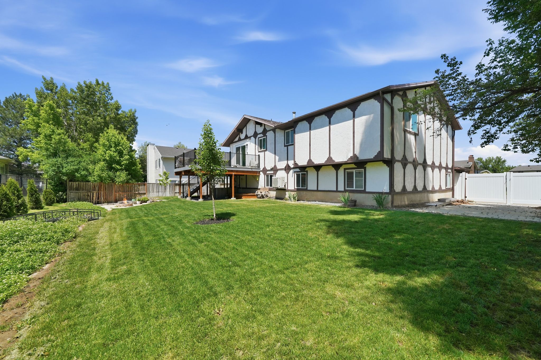 Expansive rear yard featuring a wood-tone deck, manicured lawn, and mature trees