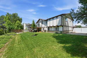 Expansive rear yard featuring a wood-tone deck, manicured lawn, and mature trees
