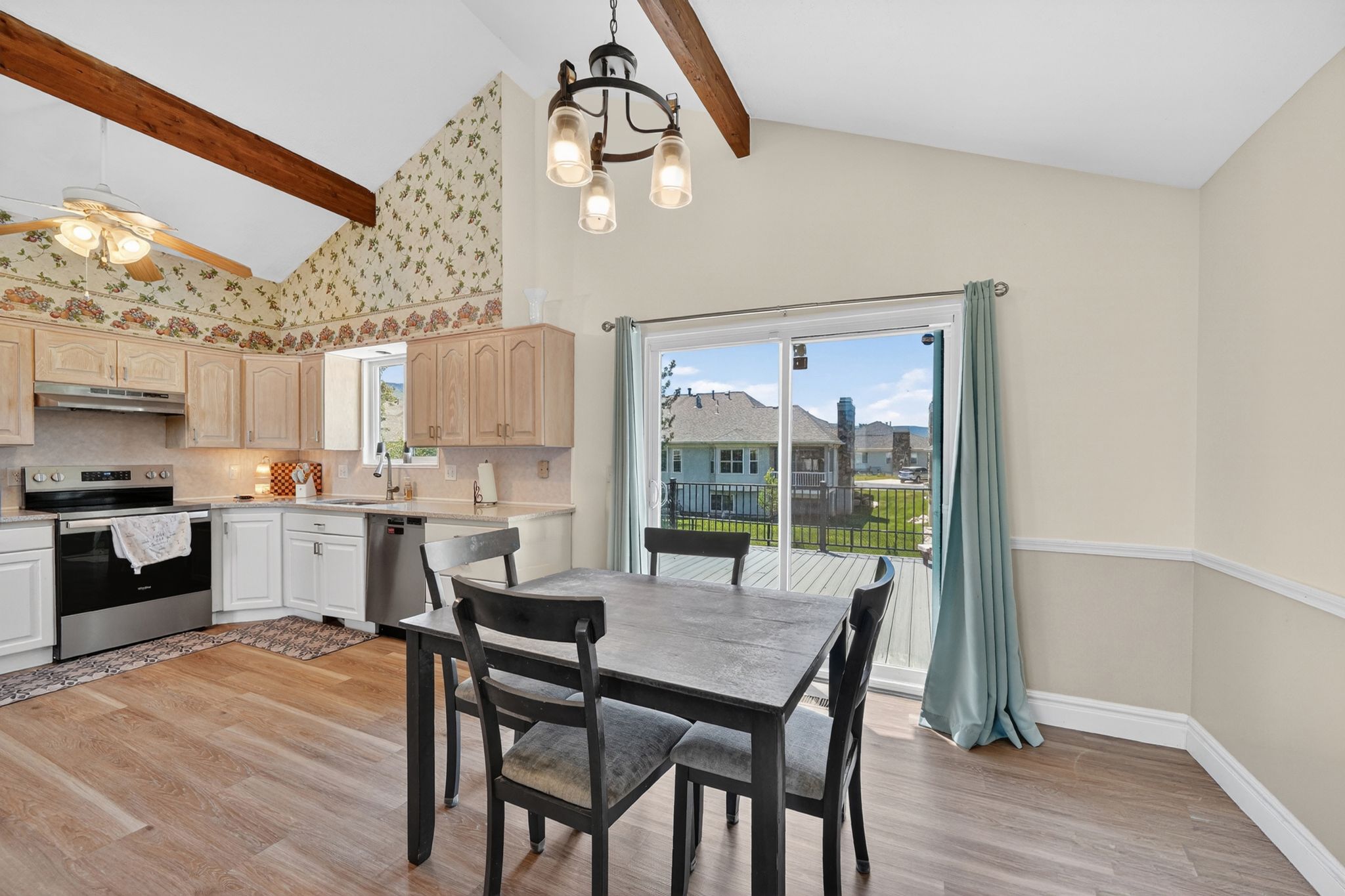 Vaulted ceiling kitchen featuring exposed wood beams, light wood-finish cabinetry, stainless steel appliances, and wood-finish flooring